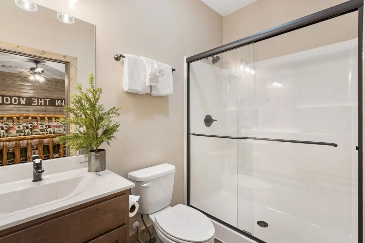 A modern ensuite bathroom featuring a vanity with a sink, a glass-enclosed shower, and a mirror with a wooden frame. The space is bright, clean, and thoughtfully designed for comfort and privacy.