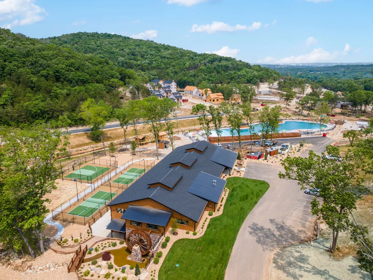 A vibrant resort amenities area featuring a recreational building, large swimming pool, tennis courts, and a mountainous landscape in the background. The open outdoor spaces and variety of activities invite families and groups to enjoy swimming, tennis, and nature walks, all within reach of the cabin.