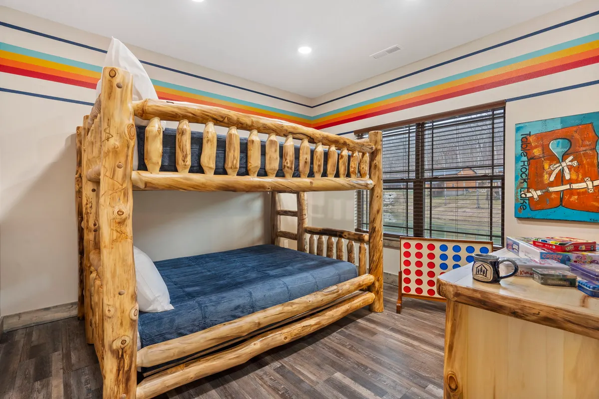 A cheerful bunk room with a queen-over-queen bunk bed, playful colorful wall stripes, and creative artwork. The space feels lively and fun, ideal for children or cousins sharing a sleepover experience.