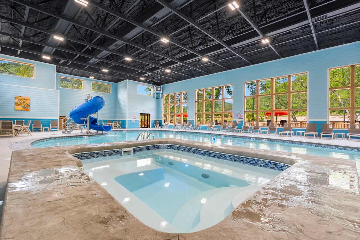 This image captures the resort's spacious indoor pool area, featuring a waterslide, a dedicated spa area, abundant natural light from large windows, and comfortable lounge chairs. The inviting atmosphere is lively, with children playing and adults relaxing, showcasing year-round aquatic enjoyment.