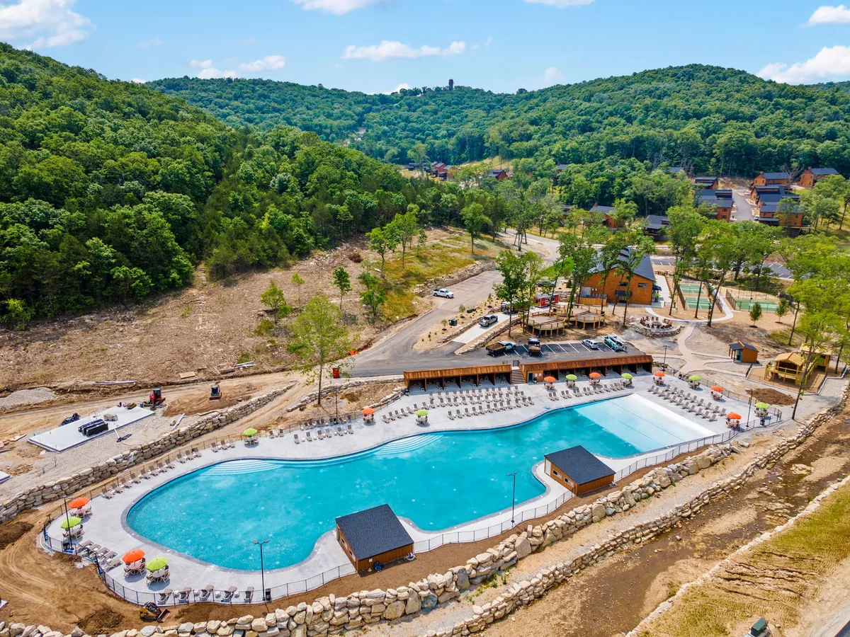An inviting exterior shot of a large swimming pool surrounded by lush greenery and lounge chairs, with buildings in the background. The pool area feels open and relaxing, ideal for cooling off after a day's adventure or soaking up the peaceful resort atmosphere.