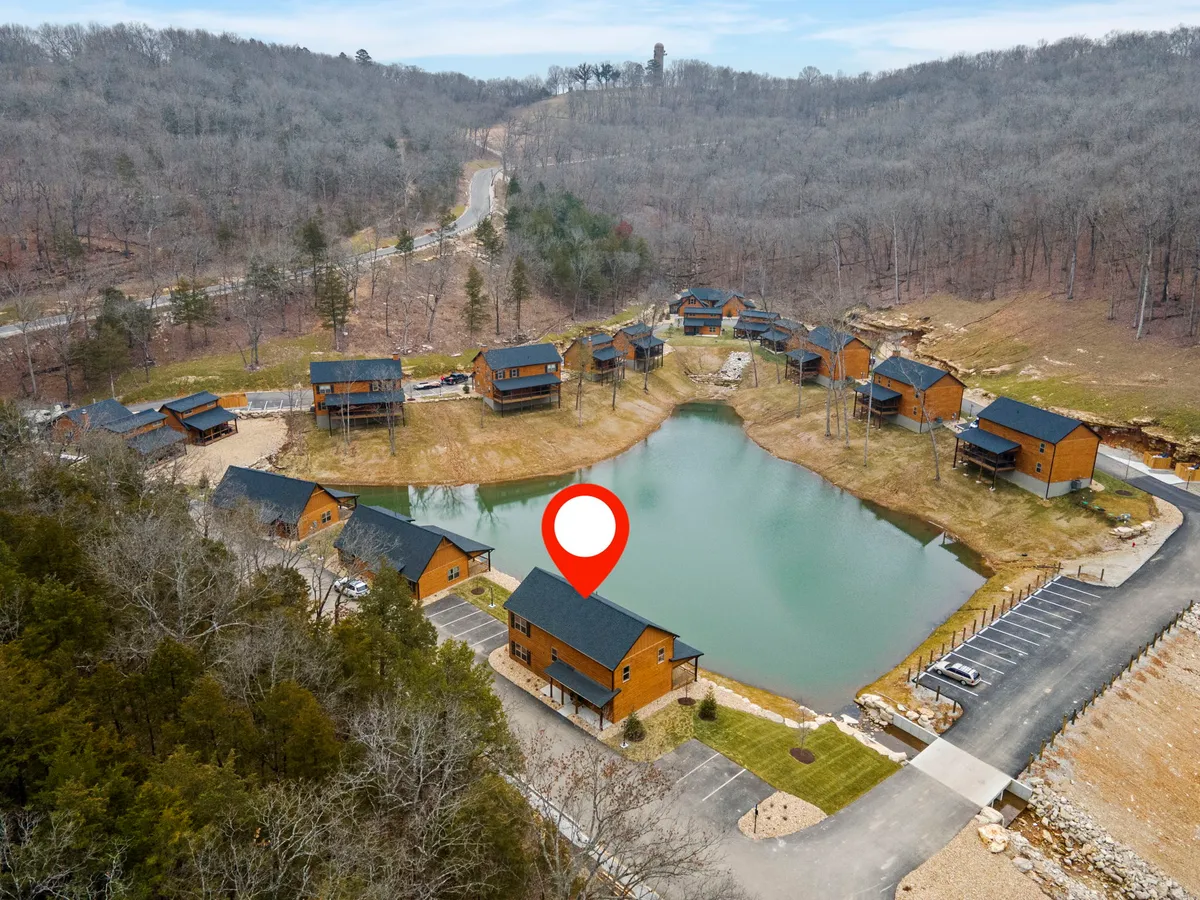 A panoramic exterior view of a lake bordered by cozy cabins and dense Ozark forest. The scene is bathed in soft, golden sunset light, with the lake reflecting the sky. The surrounding landscape hints at diverse outdoor adventures such as fishing, boating, and hiking.