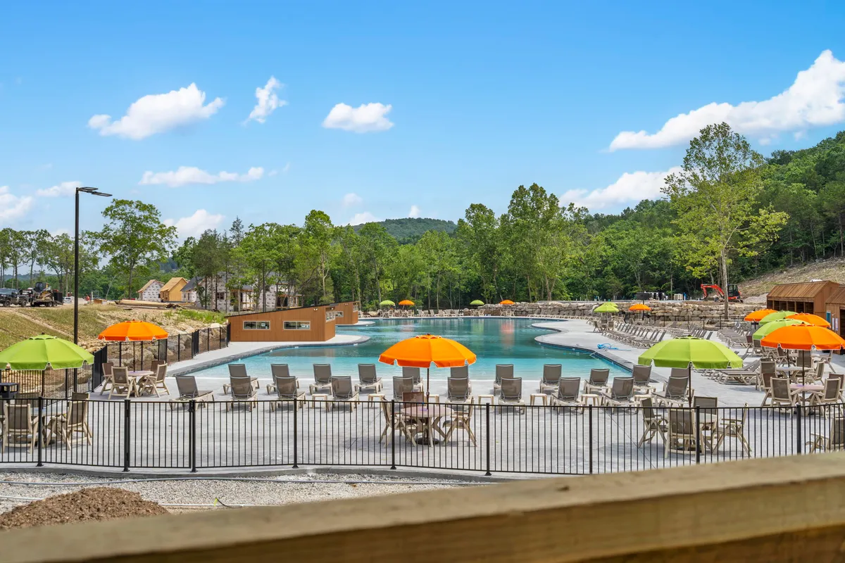 An outdoor swimming pool is surrounded by colorful umbrellas, lounge chairs, and lush trees. The lively space is ideal for swimming, sunbathing, and gathering with family and friends during warm weather, reflecting the seasonal aspect of the resort's amenities.