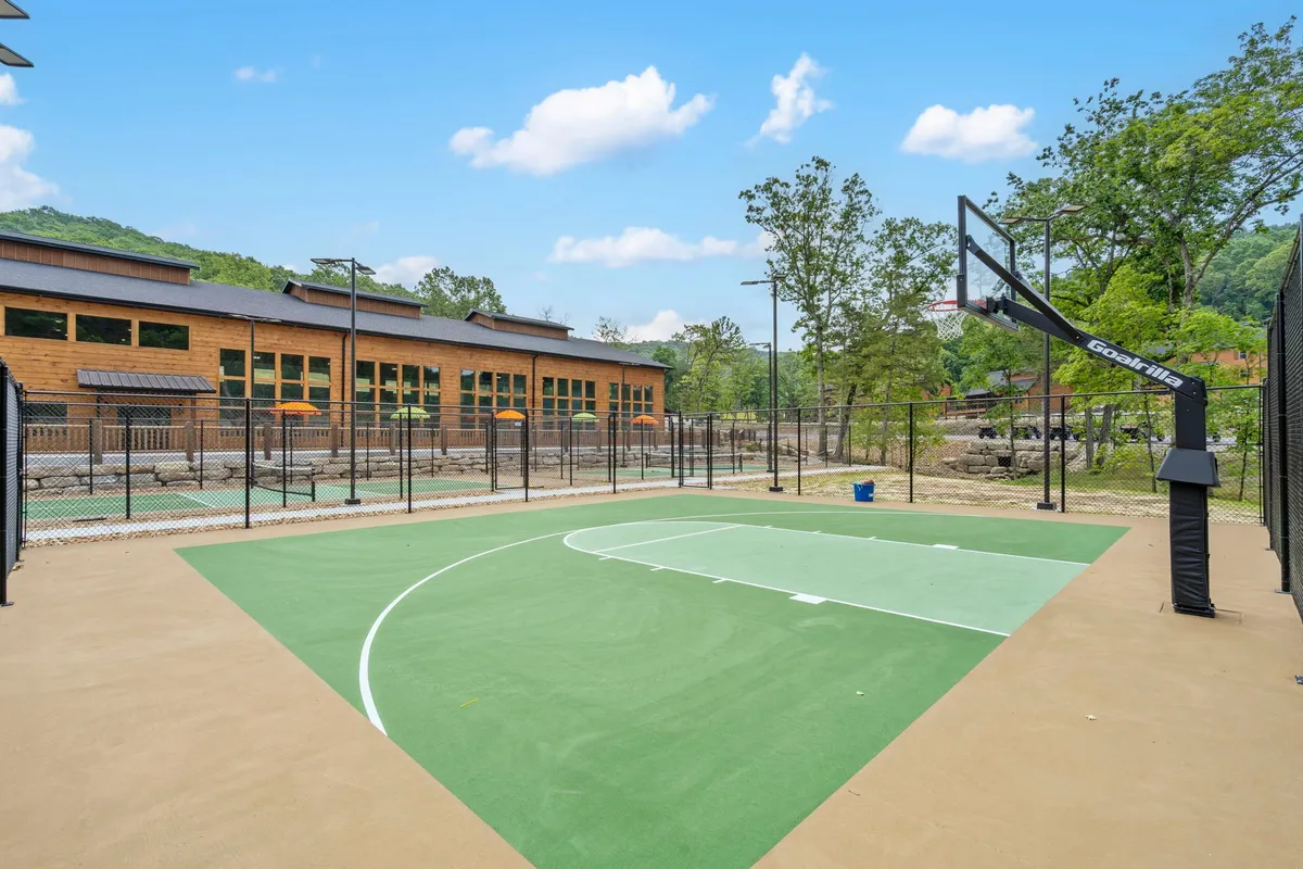 A well-maintained basketball court stands amidst tall trees with a building in the background. The court inspires active outdoor play, friendly competition, and community events, rounding out the range of resort sports amenities.