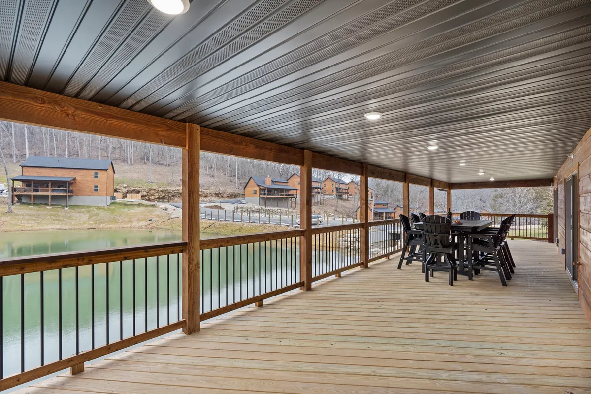 A spacious wooden deck with comfortable seating overlooks a shimmering lake, while nearby cabins nestle among the trees. The golden hues of sunset cast a warm glow, inviting relaxation and making it an ideal spot for both intimate conversations and group gatherings.